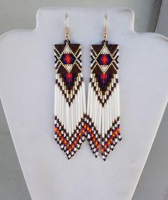 a pair of earrings with beaded designs on them hanging from a white display stand