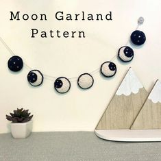 the moon garland is made with black and white yarns, which are hung on a string next to a potted succulent