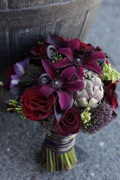 a bridal bouquet with purple and red flowers is sitting on the ground next to a potted plant