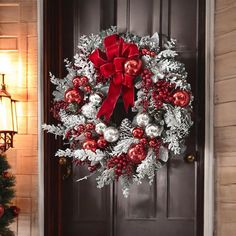 a christmas wreath on the front door with red and silver ornaments hanging from it's side