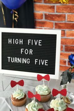 some cupcakes are sitting on a table near a sign that says high five for turning five