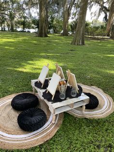 three chairs and two tables in the grass with black cushions on them, near some trees