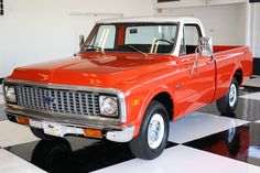 an old red pickup truck is parked on a black and white checkerboard floor