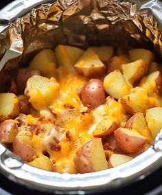 a crock pot filled with potatoes and cheese on top of an aluminum foil wrapper