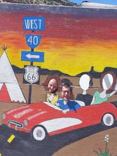 two people are sitting in a red sports car painted on the side of a building