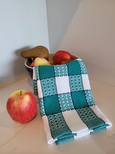 two apples and an avocado in a bowl on a counter next to a dish towel