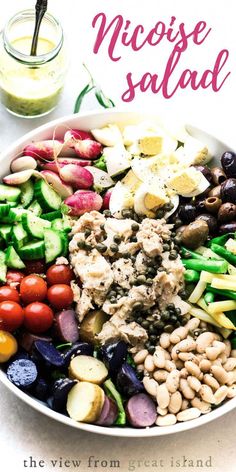 a bowl filled with lots of different types of vegetables and meats next to a jar of dressing