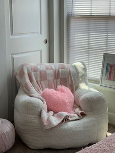 a pink heart shaped pillow sitting on top of a white chair next to a window