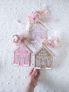 a hand holding up three small gingerbread house magnets on top of a table