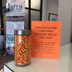 a jar filled with candy corn next to a sign that says can you guess how many candies are in the jar?