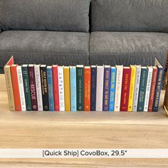 a stack of books sitting on top of a wooden table next to a gray couch