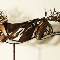 a sculpture made out of metal and wood with hair on it's head, sitting against a white wall