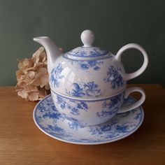 a blue and white tea set sitting on top of a wooden table next to dried flowers