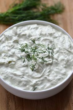 a white bowl filled with sour cream and topped with fresh dill sprigs