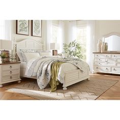 a white bed sitting on top of a wooden floor next to a dresser and mirror