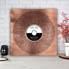 a personalized copper record with the names and date printed on it, in front of a brick wall