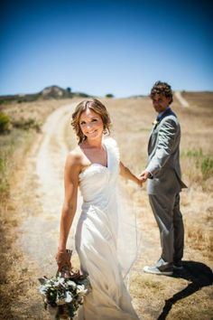 a bride and groom holding hands on a dirt road