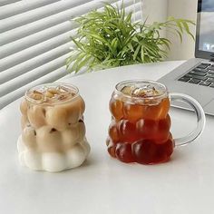 two mugs filled with liquid sitting on top of a table next to a laptop