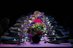 a long table is set with purple and pink flowers, black napkins, and silverware