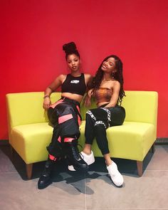 two young women sitting on a yellow couch in front of a red and orange wall