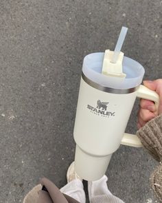 a person holding a white coffee cup with a straw in it's mouth while standing on the sidewalk