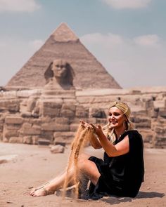 a woman sitting on the ground next to a dog in front of an egyptian pyramid