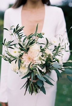 a woman holding a bouquet of flowers and greenery on her wedding day in the grass