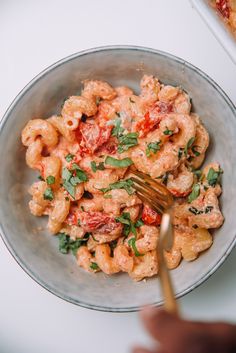 a bowl filled with pasta and sauce on top of a white table next to a fork