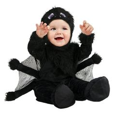 a baby dressed in a costume sitting on the floor with his hands up and eyes wide open