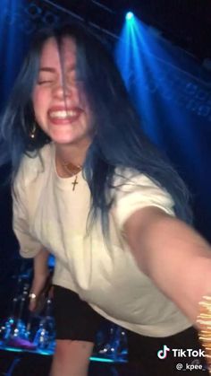 a woman with blue hair is smiling and holding a cell phone in her hand while sitting on a stage