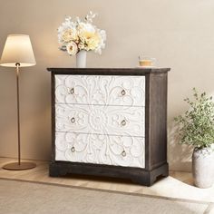 a white and brown dresser sitting on top of a wooden floor next to a lamp