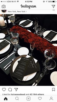 the table is set with black and white plates, silverware, and red roses