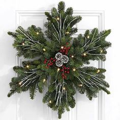 a wreath hanging on the front door of a house with red berries and pine cones