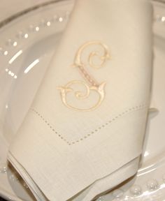 a white plate topped with a napkin and two silver plates covered in cloth monogrammed napkins