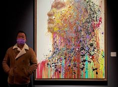 a man wearing a face mask standing in front of a painting