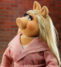 the miss piggy doll is standing in front of a brick wall wearing a pink coat