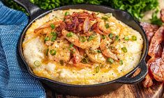 a skillet filled with mashed potatoes topped with bacon and green onions on a wooden cutting board