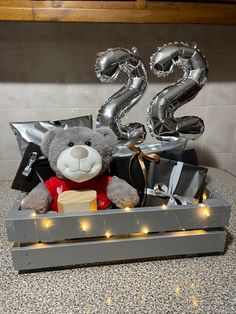 a teddy bear in a crate with balloons and gifts