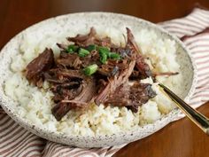 a white bowl filled with rice and meat on top of a wooden table next to a fork