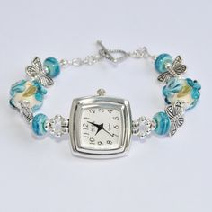 "This elegant Blue Floral lampwork beaded watch features a custom made watch face. This watch is 6 1/2\" to6 3/4\" \" long (Using the EZ Bracelet). The watches are Geneva Brand watch faces that was custom made for another jeweler that used to make beaded watches which included his stylized TikTok logo. The other specs for these watches are: Sterling silver plating on the case, custom designed raised silver numerals ,custom designed hour and minute hands, high quality metal Japan Miyota movement (Citizens) and a new battery. The butterflies are pewter. All the lampwork beads were made by SRA lampwork Artists. The heart toggle is Bali silver." Purple Beaded Bracelets With Watch, Diy Watch Band, Beaded Watches Bracelet, Craft Bracelets, Watches Bracelets, Tiktok Logo, Beaded Watches, Bracelet Watches Women, Bali Silver