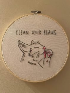 a close up of a embroidery on a wall with a cat and dog saying clean your beans