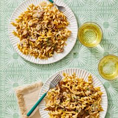 two white plates filled with pasta and mushrooms on top of a green tablecloth next to wine glasses