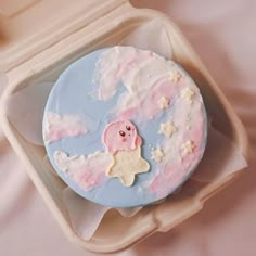 a pink and blue cake in a box on top of a white sheet covered table