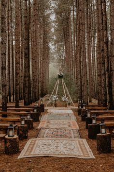 an outdoor ceremony setup in the woods with rows of benches and rugs on the ground