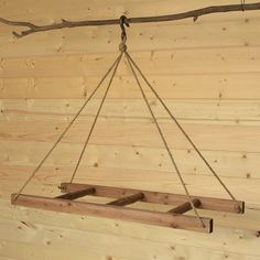 a wooden swing hanging from a tree branch in a room with wood walls and planks