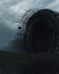 a large metal structure sitting in the middle of a field next to a body of water