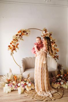 a woman holding a baby standing in front of a couch with flowers and candles around her