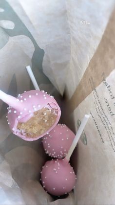 two pink cake pops with white sprinkles on them in a wrapper