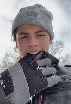 a young boy wearing gloves and holding his hand up to his mouth while standing in the snow