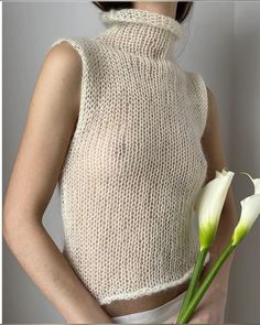 a woman holding a white flower in her right hand and wearing a knitted top